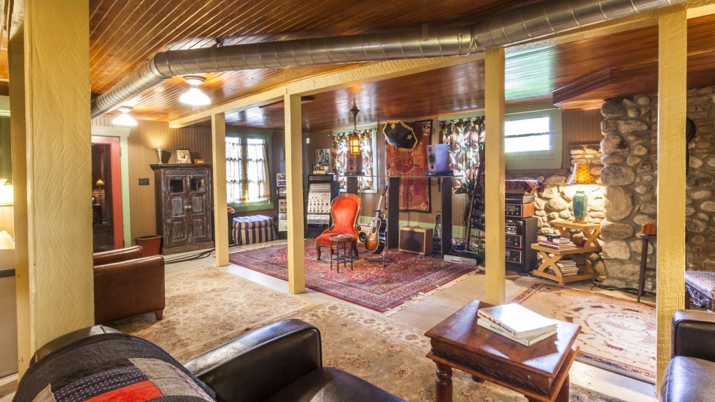Finished basement with exposed beams, stone chimney, wood paneling, vintage audio equipment, and Oriental rugs on concrete