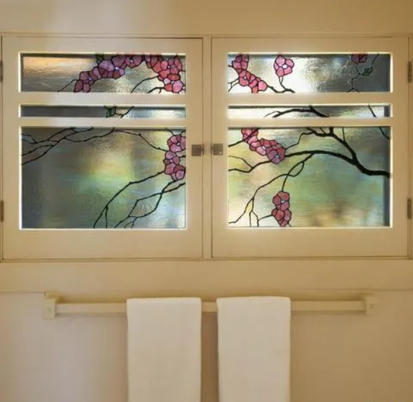 A close-up of a leaded art glass window with a green and white floral design in a bathroom.