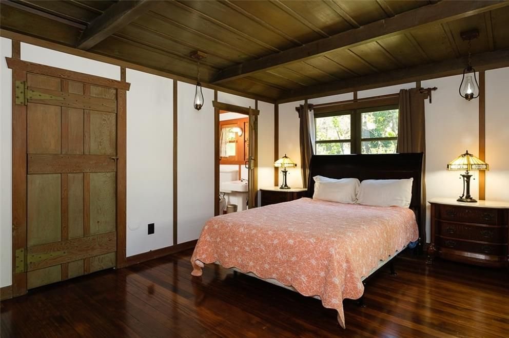 Gallery of two images showing the Edgar W. Camp House private spaces: a bathroom with exposed beam ceiling, custom wood cabinetry, and period-appropriate fixtures, and a bedroom featuring exposed structural beams, rustic wood doors, and Arts and Crafts lighting.