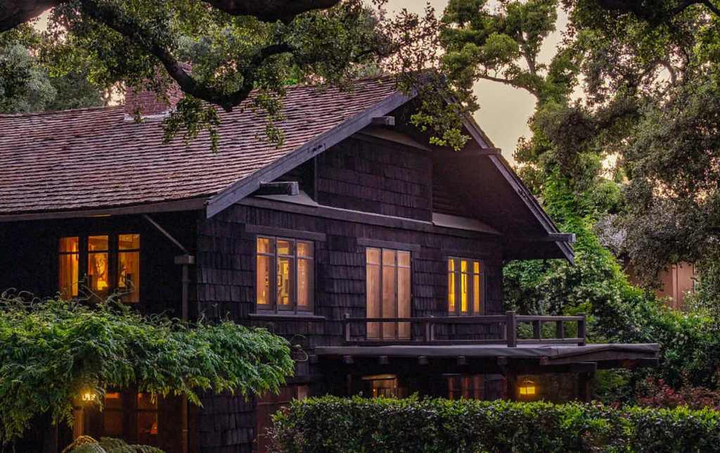 Close-up side yard view of the Louise C. Bentz House with wood shingle siding, windows, and mature garden plantings