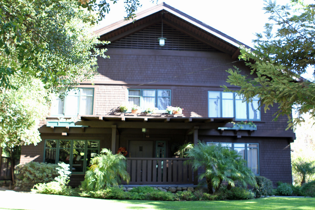 Gallery of four contemporary photographs showing the Josephine van Rossem House No. 2 (1904) by Greene & Greene, including driveway approach view, front door entrance detail, full front elevation, and covered front porch, demonstrating the California House concept with cedar shingle siding, cobblestone foundation, and mature landscape integration in Pasadena, California.