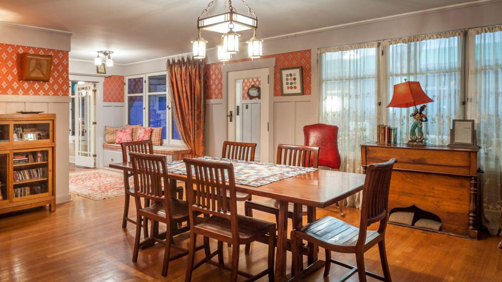 Dining room with Mission-style table and chairs, orange geometric wallpaper, Arts and Crafts chandelier, and built-in sideboard