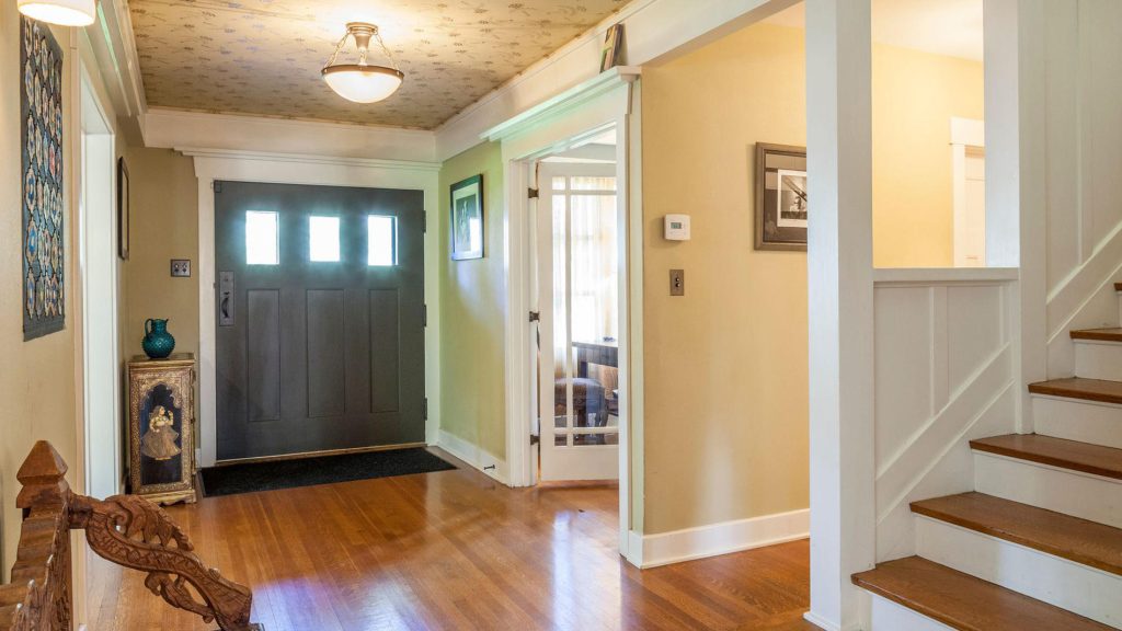 Entryway with dark green Arts and Crafts door, decorative ceiling, hardwood floors, and view to staircase and living room