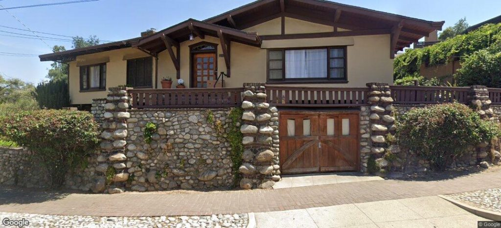 Full street view of Martha, Violet and Jane White House displaying complete Arts and Crafts composition with boulder stone foundations, wooden balustrades, and integrated roof planes by Greene & Greene, 1903.