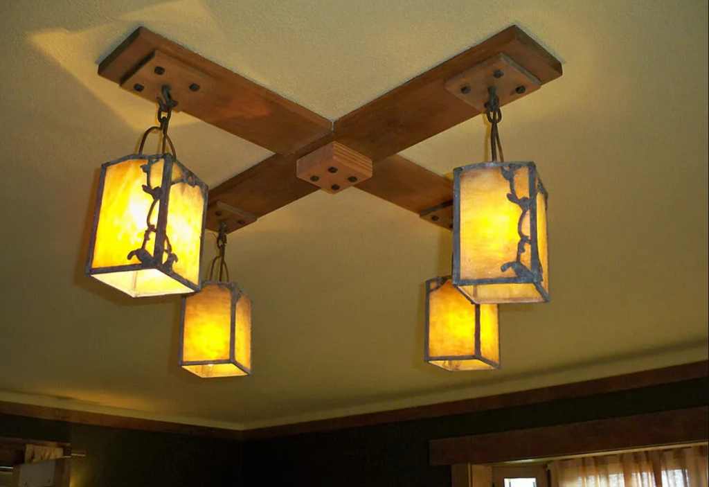 A close-up photograph of a custom-designed light fixture in the Miss Lucy E. Wheeler House, showing its delicate metalwork and art glass shade.