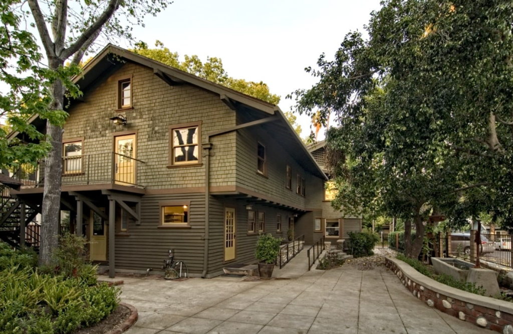 Rear elevation of the Samuel P. Sanborn House showing the angled wing configuration with shingled siding, exposed structural elements, and integration with mature landscaping.
