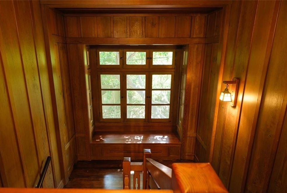 Interior view of the Edgar W. Camp House stairway showing rich wood paneling, built-in window seat with multiple glass panes, and Arts and Crafts lighting fixtures.