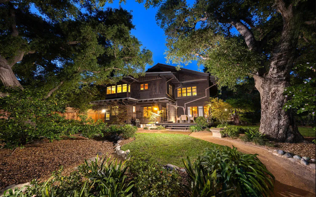 Twilight backyard view of the Louise C. Bentz House with illuminated windows, patio, pergola, and mature landscaping