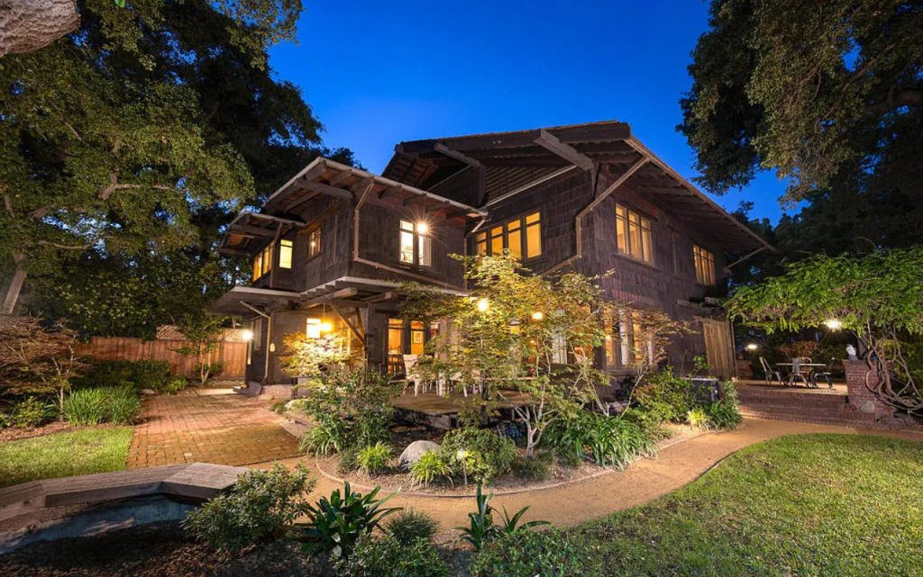 Twilight side yard view of the Louise C. Bentz House showing illuminated windows, wood siding, and mature landscaping