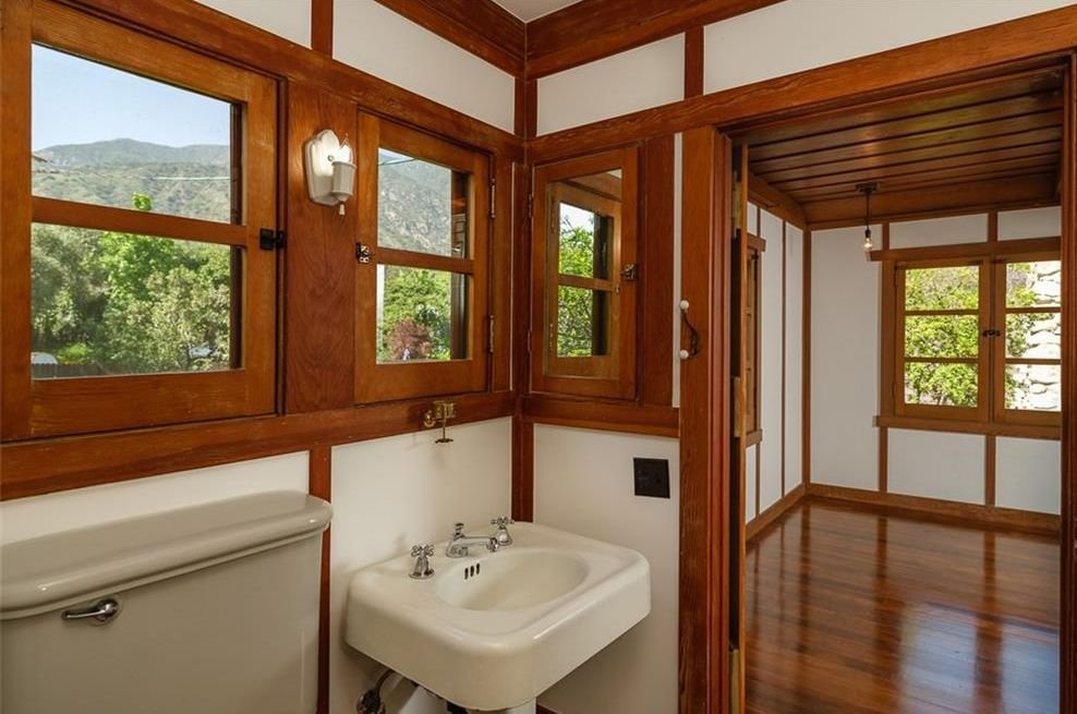 Gallery of two images showing the Edgar W. Camp House upstairs spaces: a bathroom with extensive wood trim, casement windows offering mountain views, and period fixtures, and a bedroom featuring exposed beam ceiling, built-in wood cabinetry, and comprehensive wood millwork throughout.