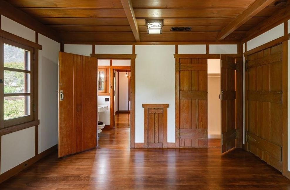 Gallery of two images showing the Edgar W. Camp House upstairs spaces: a bathroom with extensive wood trim, casement windows offering mountain views, and period fixtures, and a bedroom featuring exposed beam ceiling, built-in wood cabinetry, and comprehensive wood millwork throughout.