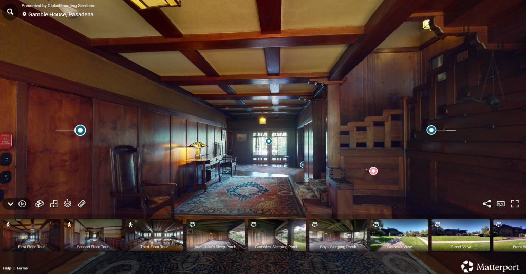 Screenshot of the Gamble House interactive virtual tour interface presented by Global Imaging Services and Matterport, showing the second floor hall with Honduras mahogany wall paneling, exposed beam ceiling with cream-colored plaster between dark-stained beams, built-in staircase with geometric balustrade at right, Arts and Crafts carpet with floral pattern, pendant light fixture with amber glass shade, and views through to other rooms, with interactive navigation points marked by colored circles, and thumbnail images at the bottom showing different tour locations including First Floor Tour, Second Floor Tour, Third Floor Tour, Aunt Julia's Sleep Porch, Gambles' Sleeping Porch, Boys' Sleeping Porch, Sidewalk View, Street View, and Front View, demonstrating the comprehensive digital documentation of the house available for remote exploration