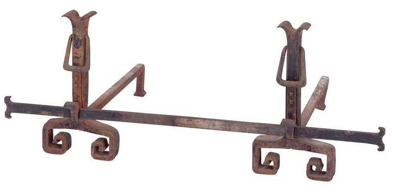 Bronze andirons with decorative crossbar positioned in fireplace, showing complete fireplace accessory ensemble. The set demonstrates unified design approach with sculptural forms and quality metalwork characteristic of Greene and Greene's collaboration with skilled artisans.