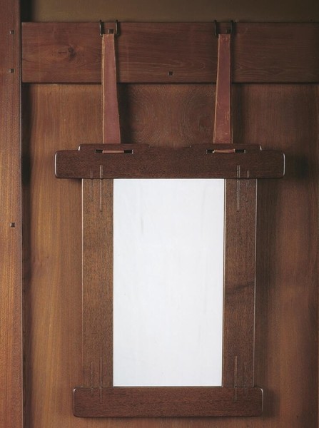 Honduras mahogany mirror frame with Arts and Crafts joinery details including visible dowels and clean lines. The frame demonstrates Greene and Greene's signature craftsmanship with simple, elegant proportions and rich wood grain, mounted on wall with period lighting visible.