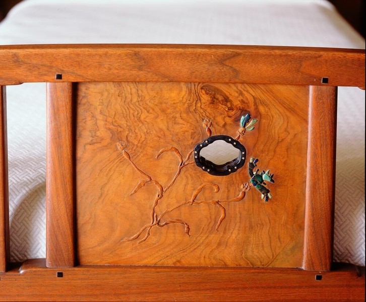Headboard detail of Gamble's bed in Honduras mahogany showcasing decorative inlay work. Features central oval abalone shell surrounded by carved organic vine motifs with turquoise and mother-of-pearl inlay accents. Visible ebony pegs at corners demonstrate signature Greene and Greene joinery craftsmanship.
