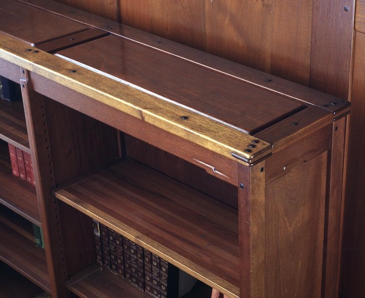 Detail of Honduras mahogany bookcase showing sliding glass door mechanism with visible brass hardware and pegs. The craftsmanship features exposed joinery, clean horizontal lines, and adjustable shelving. Rich wood grain and meticulous construction details exemplify Greene and Greene's furniture design philosophy.