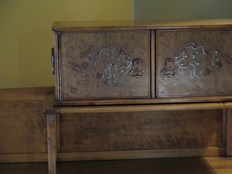 Close-up detail of the letter box compartment on a Greene and Greene designed desk at the Gamble House, showing two small drawers with figured wood panels and silver inlay depicting stylized vines with curving tendrils, custom copper hardware with cloud-lift pulls, and the characteristic square ebony pegs, demonstrating the meticulous decorative treatment applied even to small functional elements