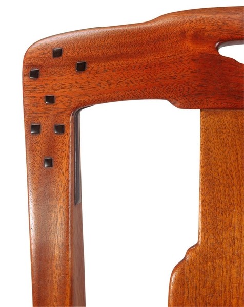 Extreme close-up detail of a Greene and Greene dining chair back from the Gamble House showing the Honduras mahogany construction with cloud-lift cutout handle, multiple square ebony pegs arranged in a geometric pattern securing the joinery, and the characteristic rounded edges and hand-rubbed finish that demonstrate the brothers' commitment to handcrafted quality and the visible expression of structural connections