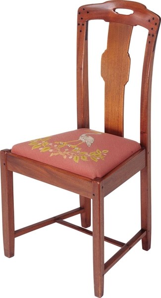 Greene and Greene designed dining room side chair from the Gamble House crafted by Peter Hall Manufacturing Company in Honduras mahogany, featuring a tall back with cloud-lift cutout handle at the crest rail, vertical splat with organic curved form, square ebony pegs securing the joinery throughout, tapered legs with stretchers, and a coral-pink silk upholstered slip seat embroidered with stylized golden oak leaves and acorns below a white heron, combining structural elegance with decorative textile arts