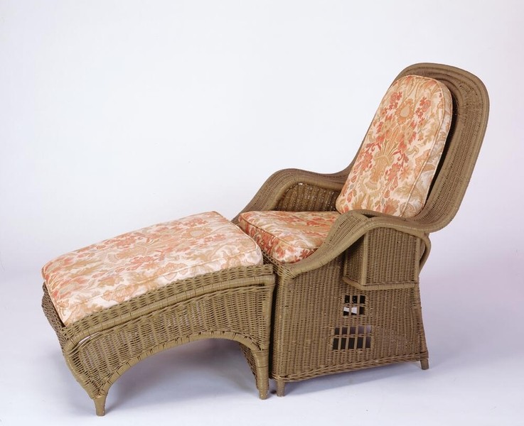 Greene and Greene designed easy chair and ottoman from Aunt Julia's bedroom at the Gamble House, crafted in soft green painted wicker with a high rounded back, rolled arms, integrated footrest extending from the seat, geometric cutout pattern in the side panels, and upholstered cushions in coral-pink fabric with stylized floral pattern in golden tones, demonstrating the brothers' use of lighter materials and finishes to create comfortable and airy spaces distinct from the heavier mahogany furniture found in the main living areas