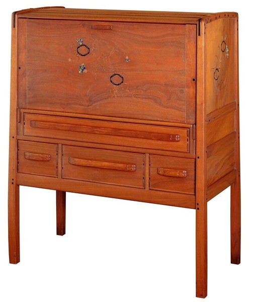 Greene and Greene designed fall-front writing desk from the Gamble House crafted by Peter Hall Manufacturing Company in Honduras mahogany, featuring a drop-front writing surface decorated with silver and abalone shell inlay depicting stylized oak leaves and acorns in an organic pattern, four small drawers below with cloud-lift copper pulls, tapered legs with square ebony pegs securing all joinery, and the characteristic rounded edges and exposed structural elements that exemplify the brothers' integration of functional design with decorative arts