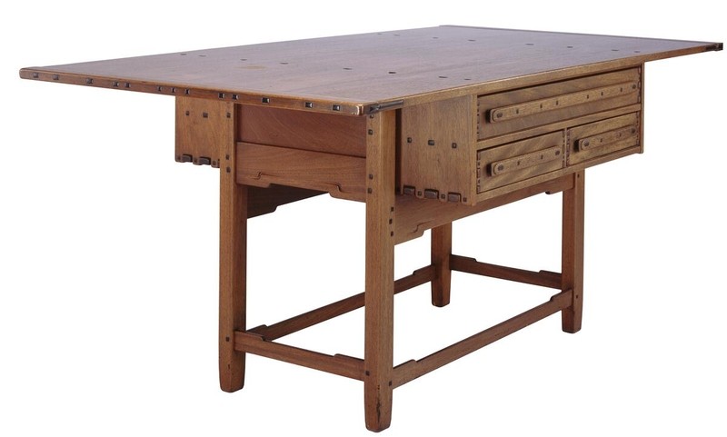 Greene and Greene designed library table from the Gamble House crafted by Peter Hall Manufacturing Company in Honduras mahogany, featuring a large rectangular top with square ebony pegs arranged in a geometric pattern around the perimeter, four drawers with cloud-lift copper pulls on one side, massive slab legs with vertical panel construction and horizontal slat cutouts, stretchers connecting the legs, and the exposed joinery and structural expressiveness that characterizes the brothers' furniture design for the ultimate bungalows