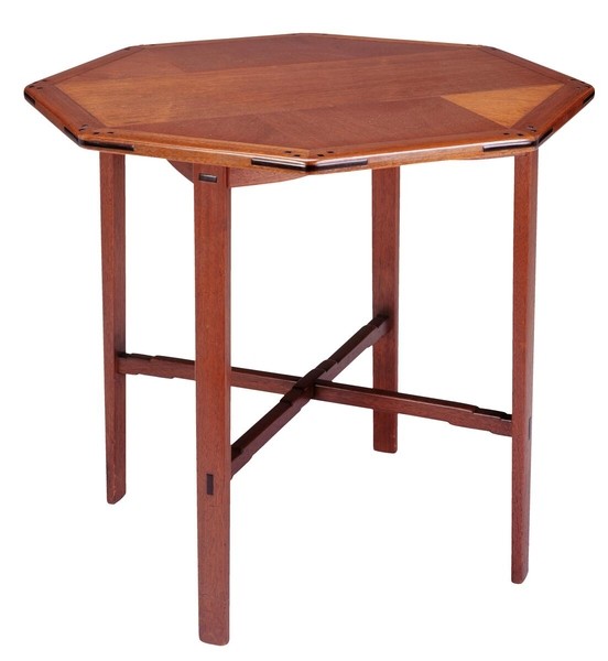 Greene and Greene designed octagonal occasional table from the Gamble House crafted by Peter Hall Manufacturing Company in Honduras mahogany and bird's-eye maple, featuring an eight-sided top with figured ebony splines at the corners forming triangular accents, square ebony pegs around the perimeter, four tapered legs with square ebony pegs, cross-stretchers connecting the legs, and the characteristic rounded edges and meticulous joinery that exemplify the ultimate bungalow furniture aesthetic