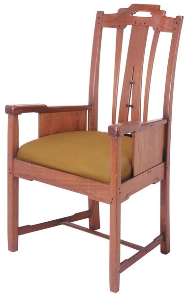 Greene and Greene designed open arm chair from the Gamble House crafted by Peter Hall Manufacturing Company in Honduras mahogany with ebony pegs, featuring a tall back with cloud-lift cutout handle at the crest rail, vertical and horizontal slats creating a geometric pattern with square ebony pegs as decorative elements, solid side panels, open arms, upholstered seat in golden-yellow leather, stretchers connecting the legs, and the characteristic exposed joinery that demonstrates the brothers' philosophy of making structural connections visible and decorative