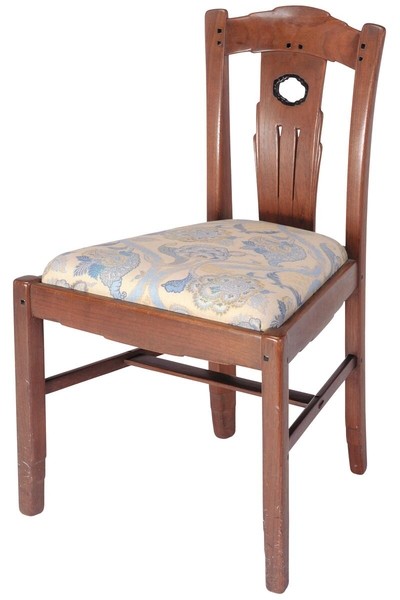 Greene and Greene designed shoe chair from the Gamble House crafted by Peter Hall Manufacturing Company in Honduras mahogany and black walnut, featuring a tall back with cloud-lift cutout handle at the crest rail, vertical splats with three linear grooves and a circular abalone shell inlay at the top, square ebony pegs throughout, stretchers connecting the legs, and an upholstered slip seat in cream fabric with stylized floral pattern in soft blue and golden tones, designed for use in the bedroom while putting on shoes