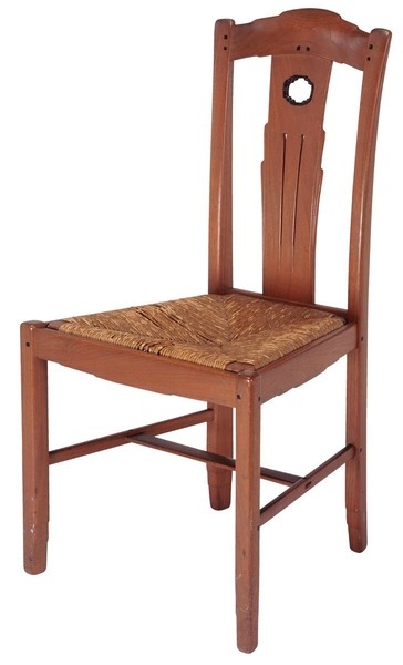 Greene and Greene designed side chair from the Gamble House crafted by Peter Hall Manufacturing Company in Honduras mahogany and black walnut, featuring a tall back with cloud-lift cutout handle at the crest rail, vertical splats with three linear grooves and a circular abalone shell inlay at the top, square ebony pegs throughout, stretchers connecting the legs, and a woven rush seat in natural golden-brown tones, demonstrating the brothers' use of traditional craft techniques combined with their signature design elements