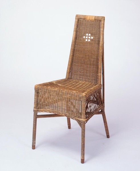 Greene and Greene designed side chair from Aunt Julia's bedroom at the Gamble House, featuring natural wicker construction with a tall back incorporating a geometric cutout pattern of small squares arranged in a grid at the upper center, tightly woven wicker seat and back panels, tapered legs, and decorative open weave pattern at the sides, demonstrating the brothers' integration of Arts and Crafts principles with lighter materials suitable for bedroom furnishings