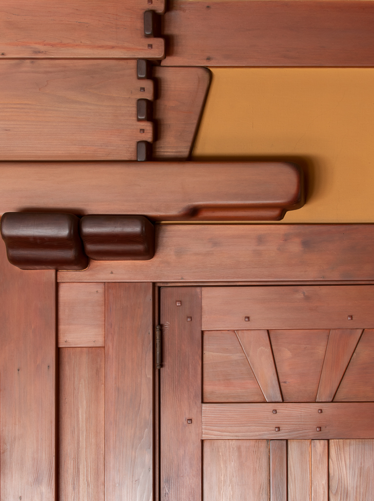 Close-up detail of Honduras mahogany trim and door joinery at the Gamble House showing the characteristic rounded edges, square ebony pegs in geometric arrangement, geometric panel designs with vertical and horizontal divisions, custom bronze door handle, and the warm golden-brown patina of aged wood demonstrating Greene and Greene's meticulous attention to detail and honest expression of materials.