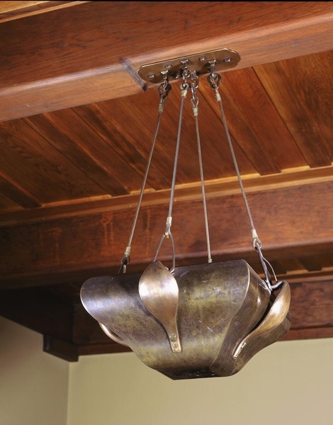 Arts and Crafts ceiling pendant light fixture suspended by chains from a brass mounting plate. The hammered metal shade features organic, petal-like forms in aged bronze or copper finish, hanging beneath exposed wooden beams with natural grain patterns characteristic of Craftsman architecture.
