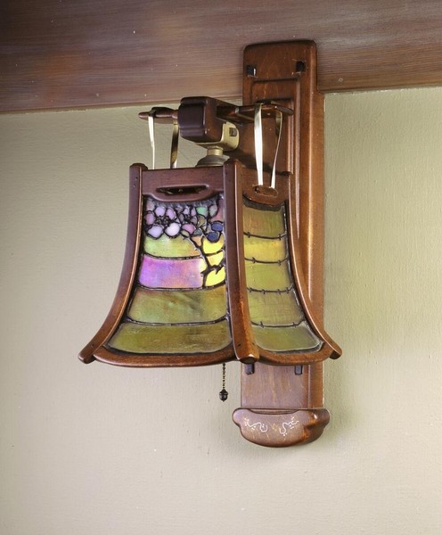 Exceptional wall sconce crafted from Honduras mahogany with silver inlay details, featuring curved organic backplate. Art glass shade displays wisteria motif in purple, yellow, and green leaded glass panels, exemplifying Greene and Greene's masterful integration of decorative arts.