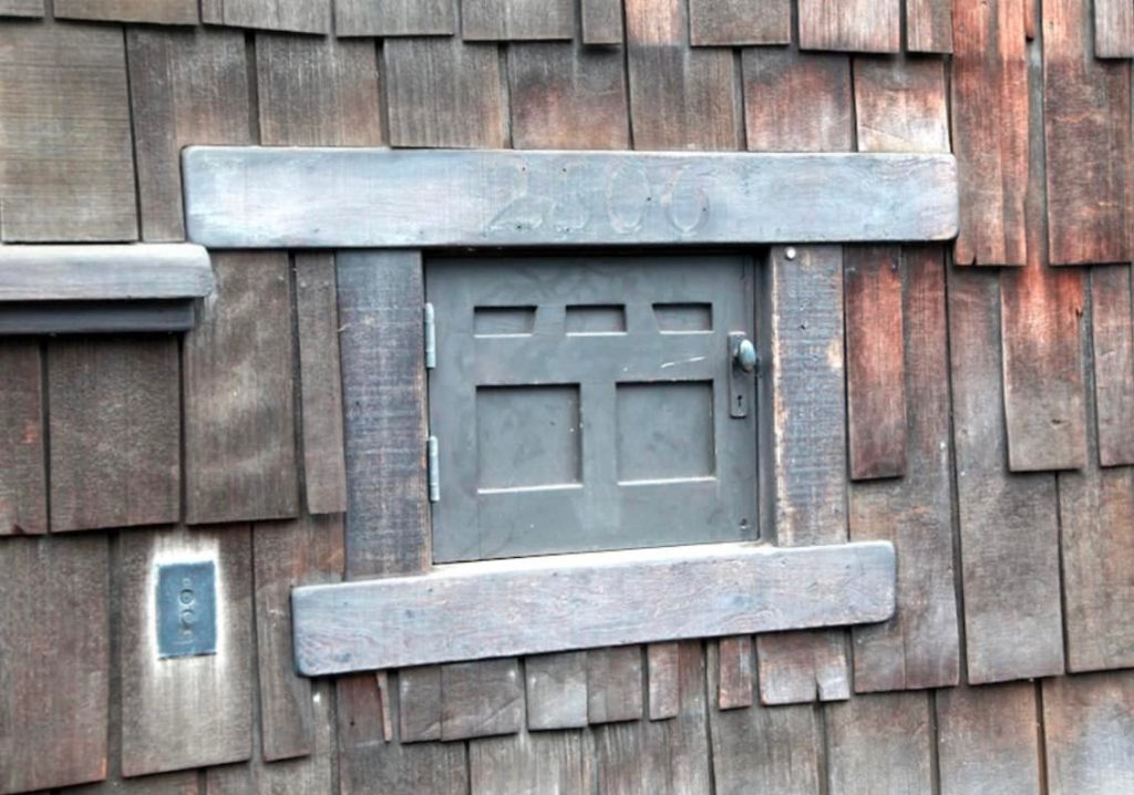 Cast-iron cold storage delivery door at Thorsen House with paneled design, metal hardware, and wood shingle surround