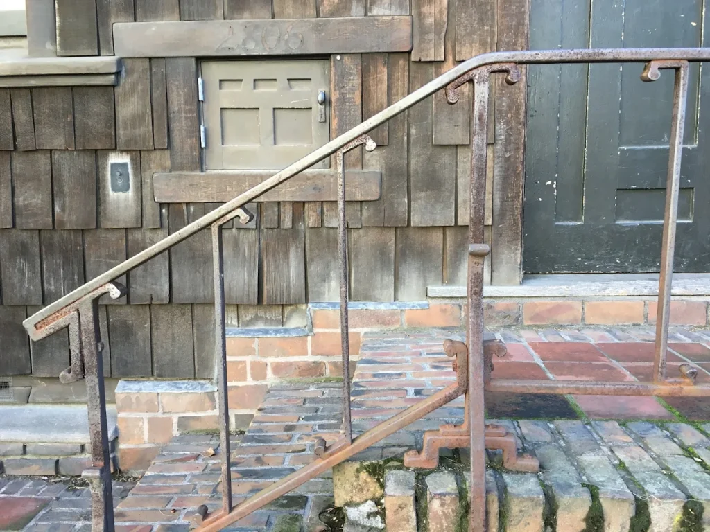 Thorsen House cold storage box with painted wood door, metal hardware, and brick stairs on wood-shingled exterior