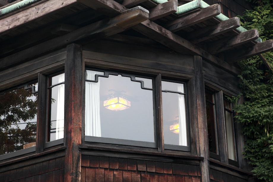 Evening view of Thorsen House dining room bay window with illuminated ceiling fixture, cloud lift art glass, and timber eaves