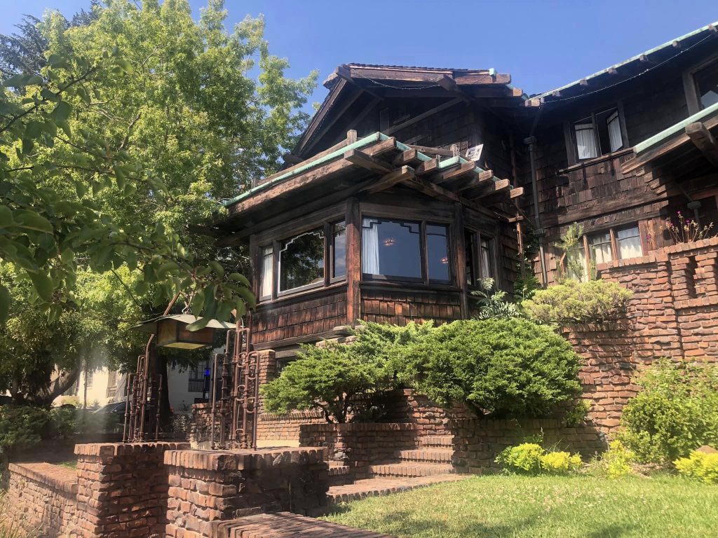 Northwest entrance showing wrought iron gate, brick stairs, bay window, and Greene & Greene timber detailing