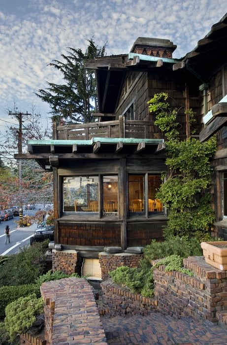 View looking north at Thorsen House entrance showing brick stairs, timber bridge, bay windows, and dramatic rooflines