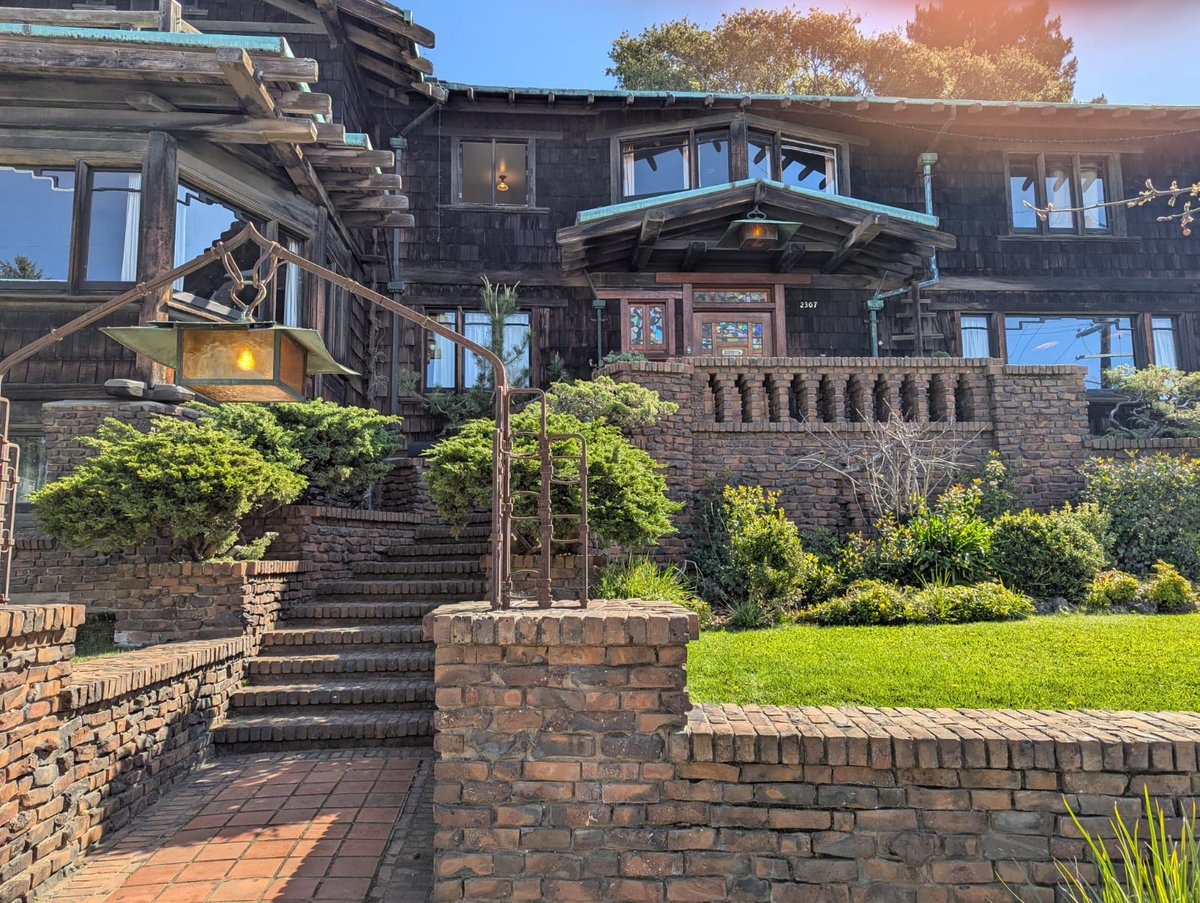 Front clinker brick entrance steps of the Thorsen House climbing from the Piedmont Avenue sidewalk between iron lanterns and brick retaining walls, with the brown-shingled facade of the house visible above