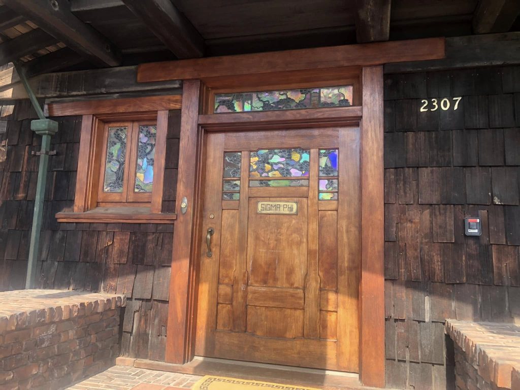 Thorsen House front door at 2307 with iridescent art glass, Sigma Phi plaque, timber frame, and copper accents
