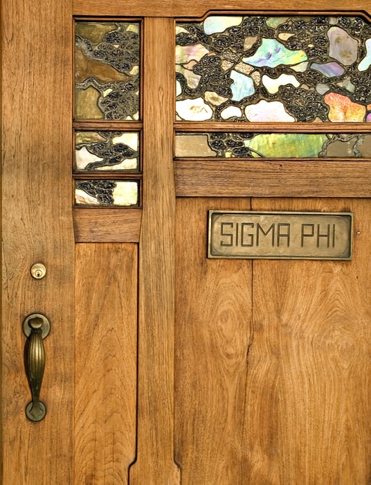Detail of Thorsen House front door showing iridescent art glass panels, Sigma Phi brass plaque, and bronze hardware