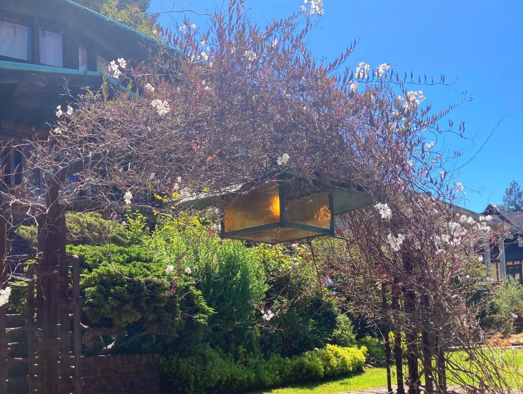 Hanging lantern on Thorsen House entrance gate with amber art glass, wrought iron frame, and spring garden setting