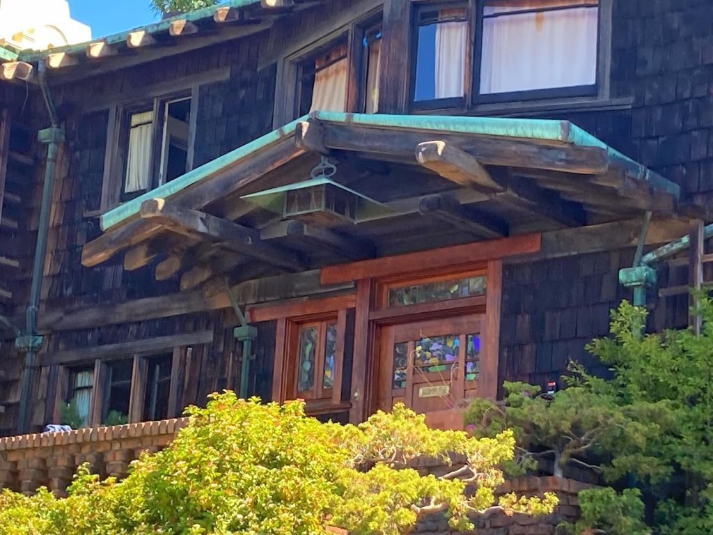 Southwest view of Thorsen House front door with art glass, timber overhang, copper accents, and clinker brick planters