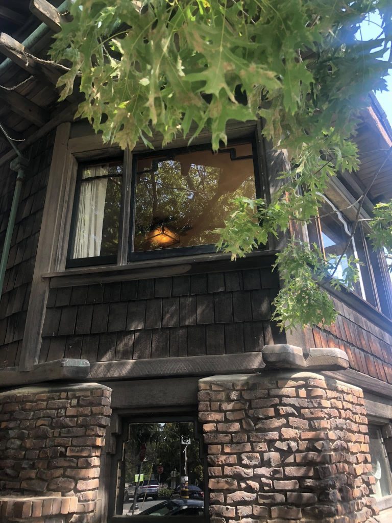 View into Thorsen House dining room through bay window showing clinker brick arches, timber frame, and interior lighting