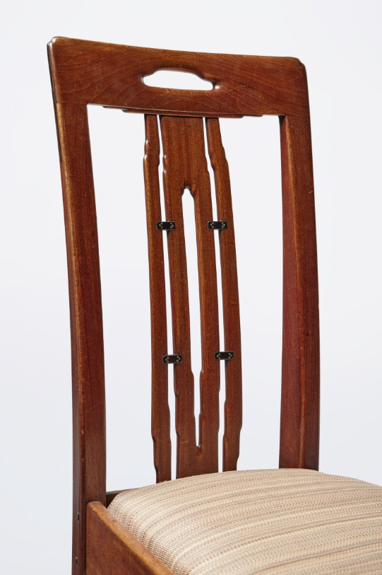 Dining chair back detail showing vertical slat design with cutout handle and ebony pegs securing joints on upholstered seat.