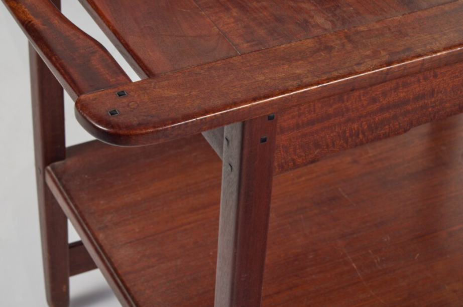 Serving table corner detail showing rounded edge with ebony pegs, shelf support joinery, and honest construction methods.