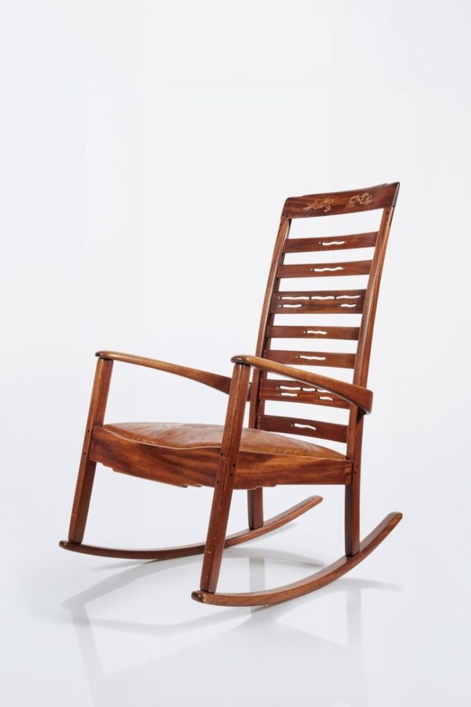 High-back rocking chair with ladder slats, floral inlay on crest rail, leather seat, and curved rockers in mahogany.