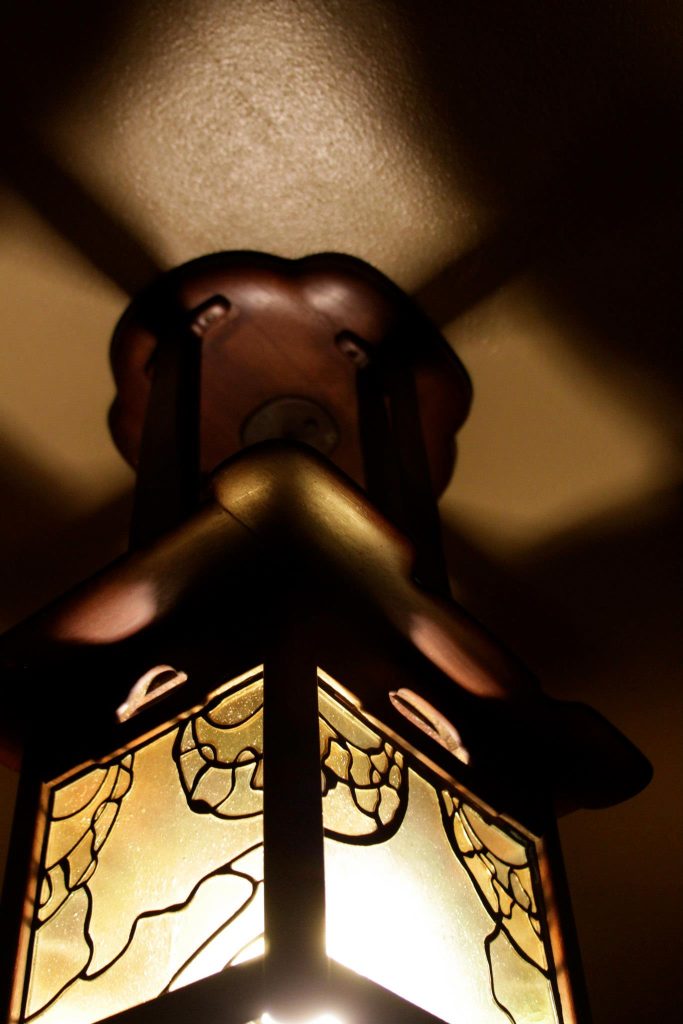Close-up of illuminated entrance hall lantern with leather straps, art glass panels, and copper hardware at Thorsen House