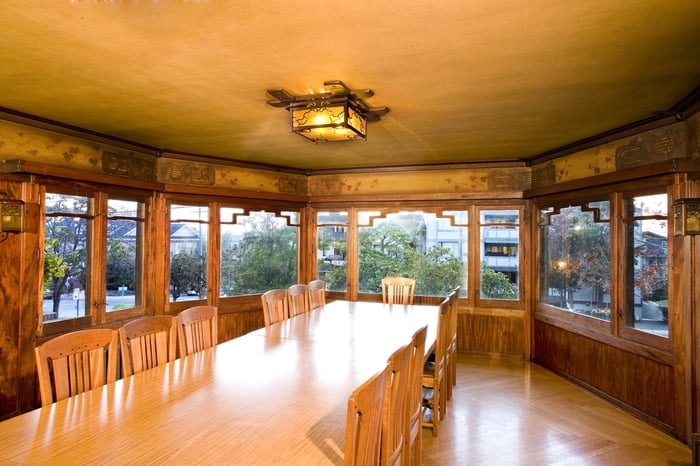 Thorsen House dining room with bay windows, original dining table and chairs, ceiling fixture, and mahogany wainscoting